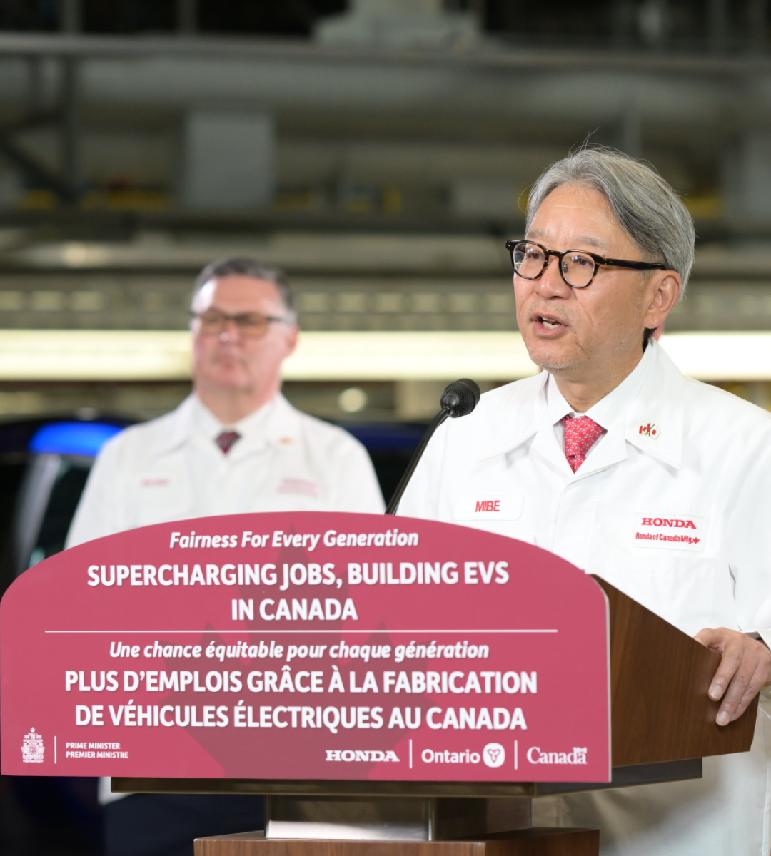 A Honda spokesperson in a white coat makes an announcement from a podium.
